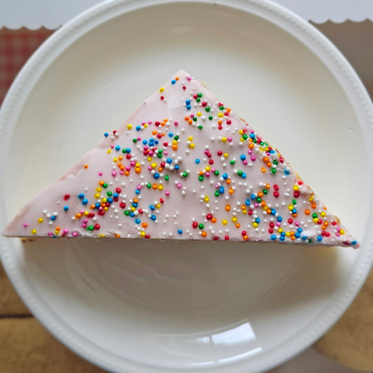 A triangular slice of cake with pink frosting and colorful sprinkles.