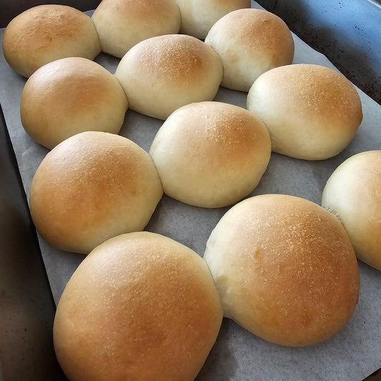 A tray of freshly baked golden-brown bread rolls on parchment paper.